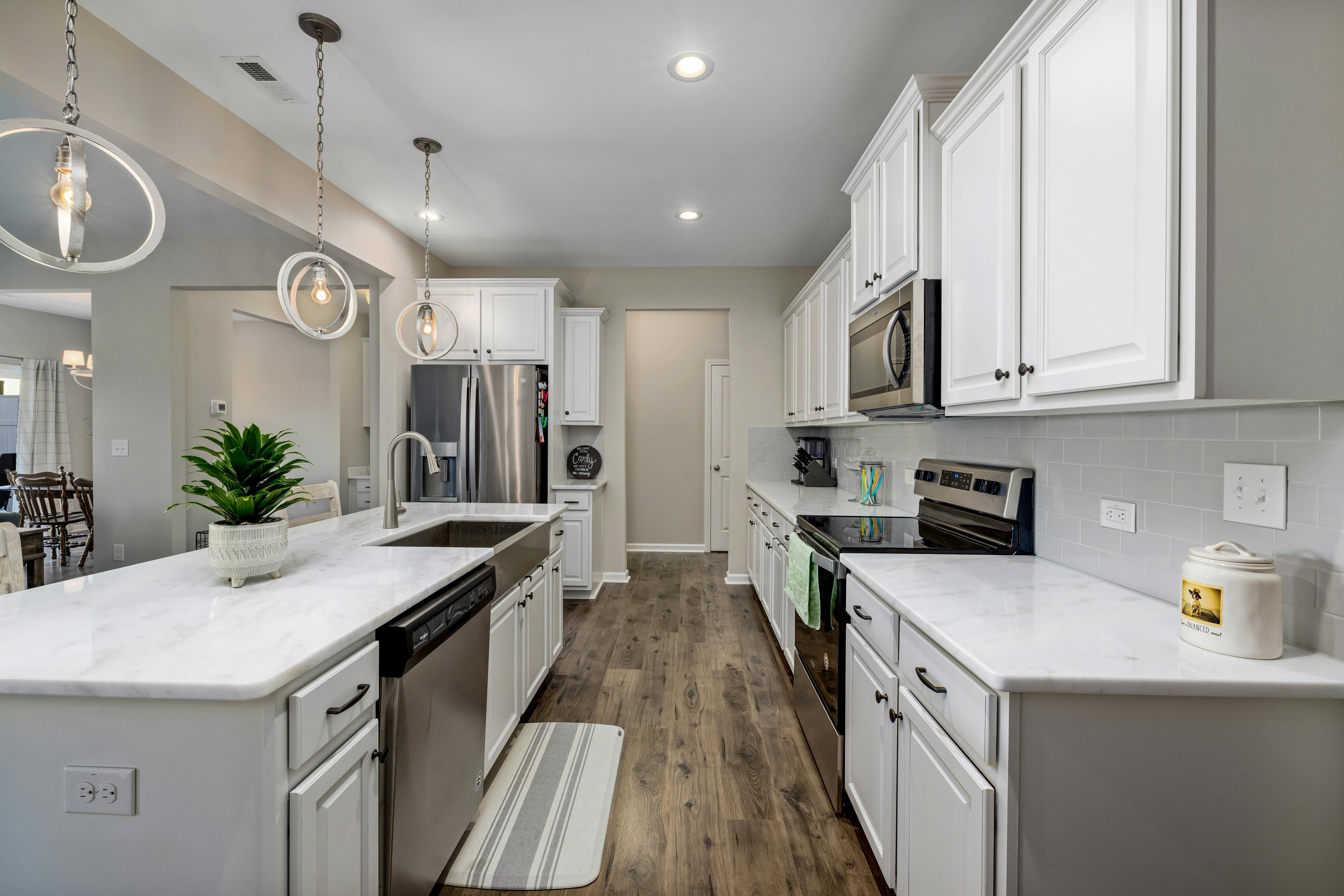 Modern, fully renovated kitchen with white cabinets, marble countertops, stainless steel appliances, and elegant pendant lighting.