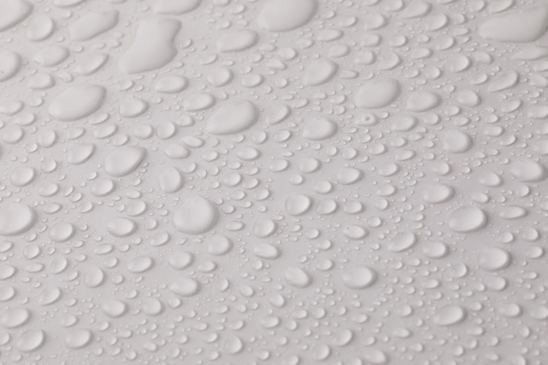 Close-up image of large and small water droplets on a white surface, representing moisture buildup or water damage.