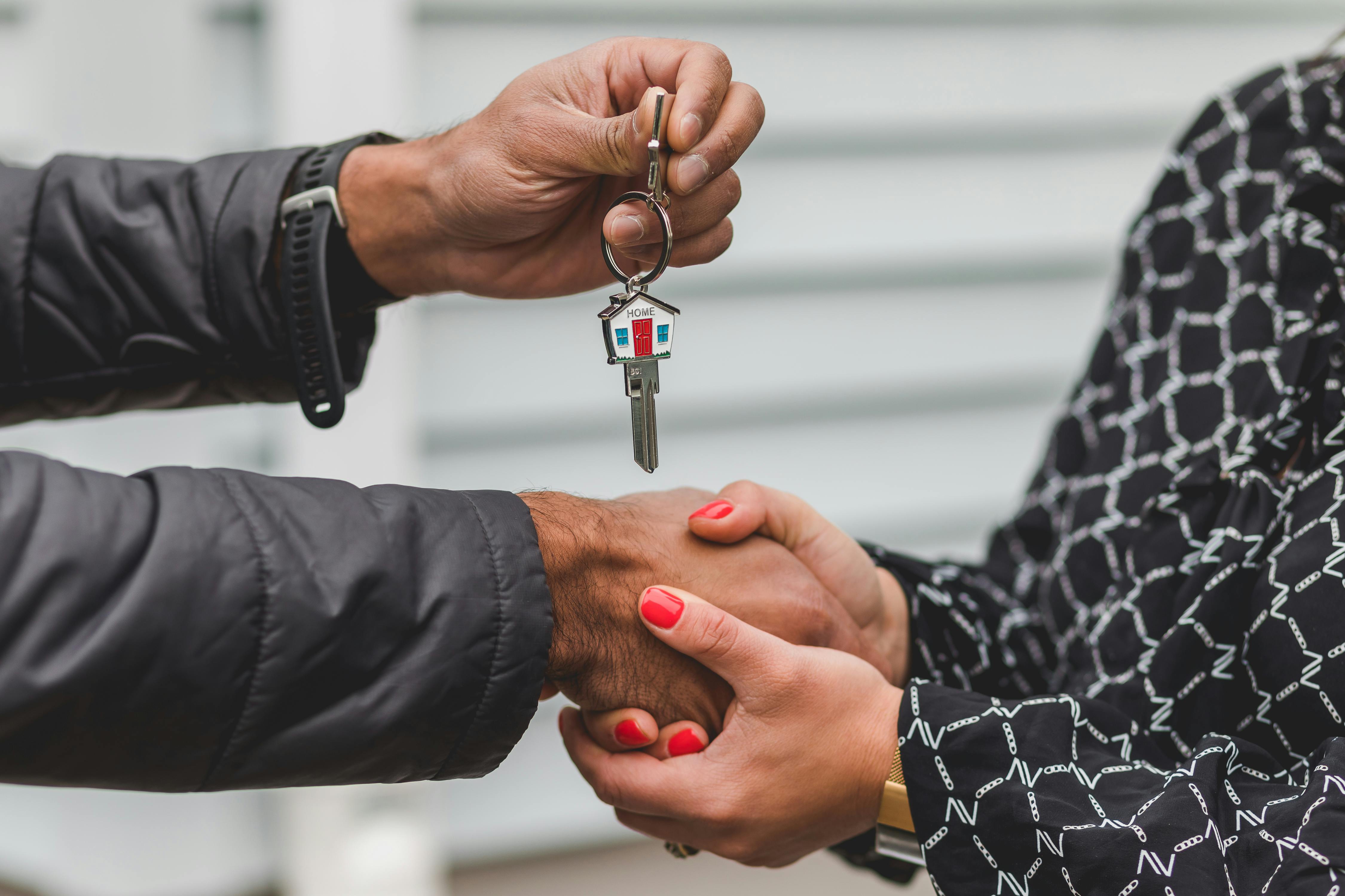 Close-up of two people shaking hands while a key with a house keychain is being handed over, symbolizing a successful real estate transaction.